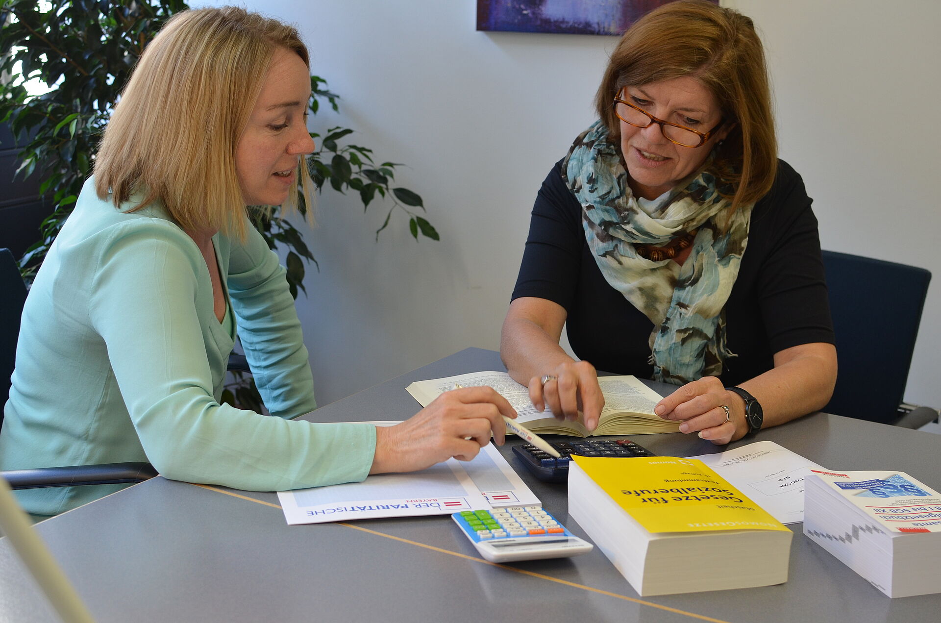 Zwei Personen in einer Beratungssituation. Vor Ihnen auf dem Tisch liegen Bücher mit Gesetzestexten.