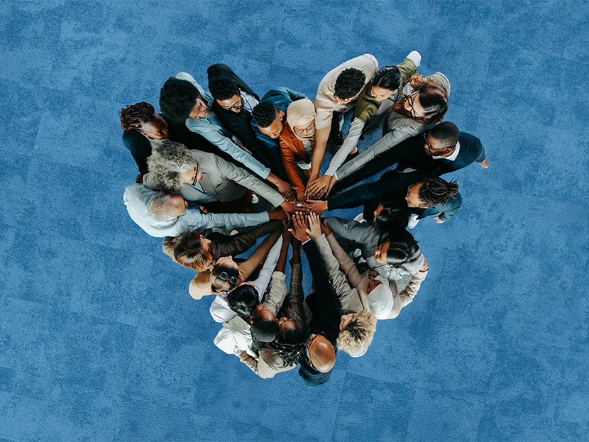 Eine Gruppe von Menschen verschiedener Herkunft hält sich an den Händen. Das Bild ist von oben aufgenommen und zeigt aus dieser Perspektive, dass die Menschen ein Herz bilden.