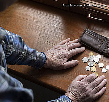 Ein älterer Mann stützt sich auf ein Fensterbrett. Vor seinen Händen liegen eine Geldbörse und kleine und größere Münzen.
