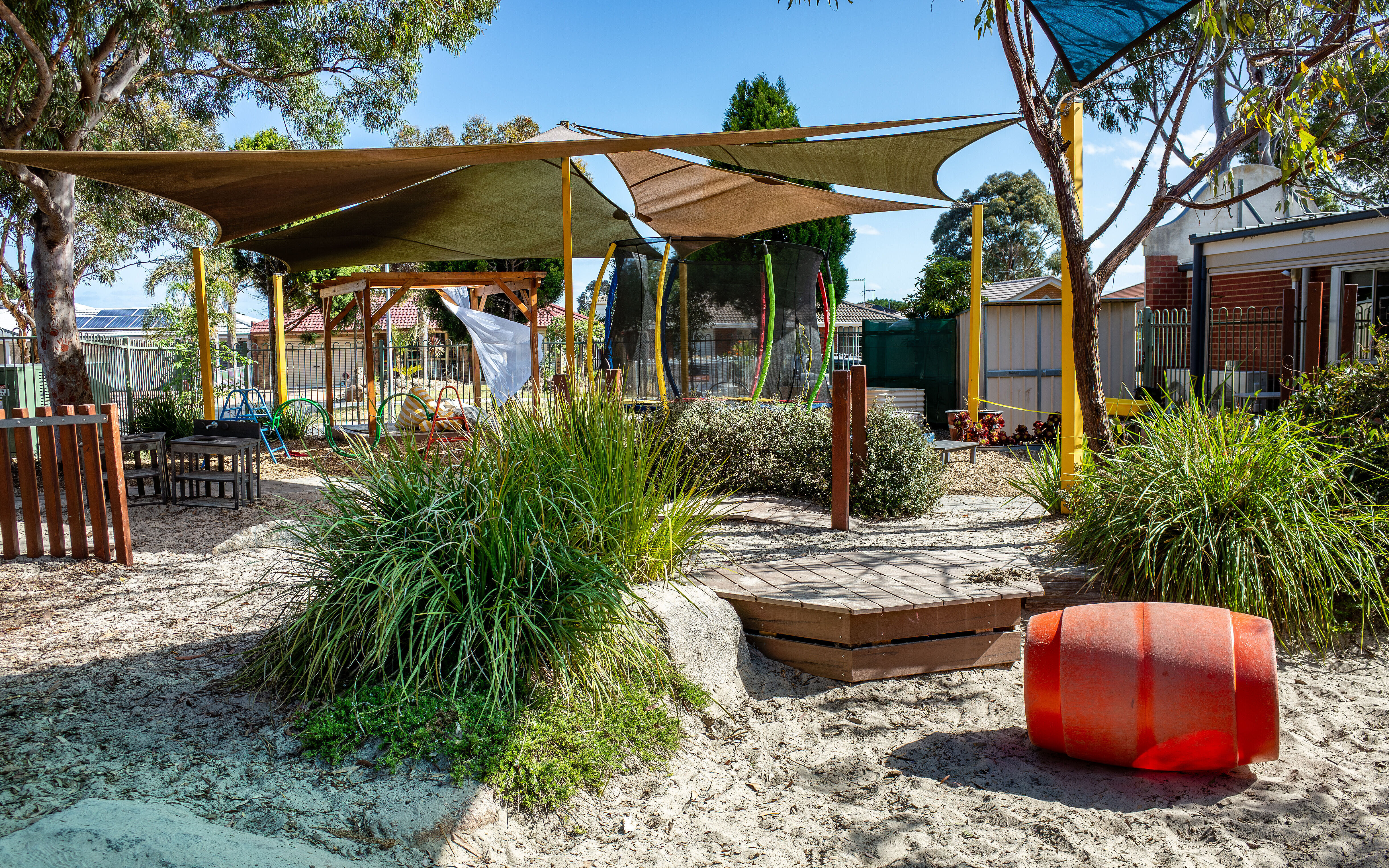 Begrünter Spielplatz mit Sonnensegeln, Sandfläche und schattigen Spielbereichen.