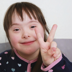 Maedchen mit Down-Syndrom zeigt das Victory-Zeichen (englisch fuer Sieg)©iStock_DenKuvaiev