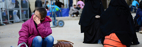 Syrisches Flüchtlingsmädchen sitzt im Flüchtlingslager auf ihren Taschen